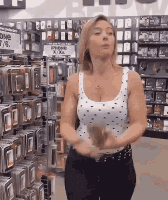 a woman in a polka dot tank top is standing in front of a display of iphone x / xs cases .