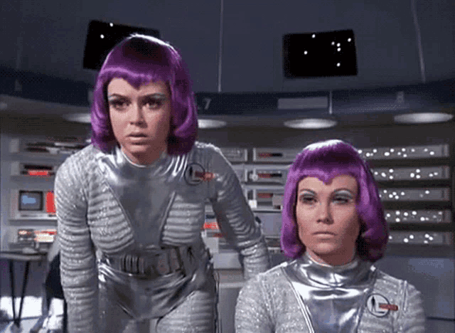 two women wearing purple wigs are standing next to each other in front of a sign that says 7