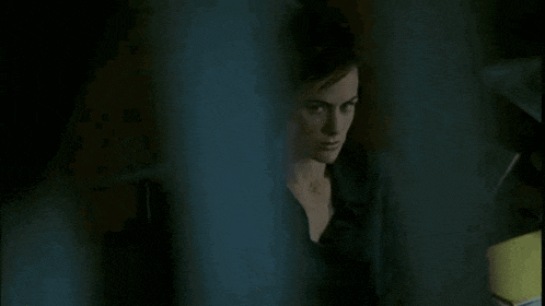 a woman is standing in a dark room behind a glass door .