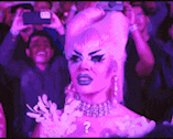 a drag queen is taking a picture of herself in front of a crowd of people .