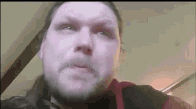 a man with long hair and a beard is looking at the camera with a sad look on his face .