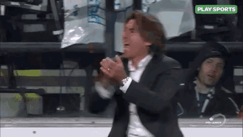 a man in a suit is applauding in front of a play sports sign