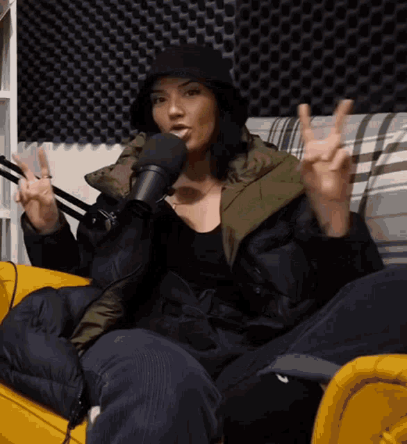 a woman wearing a black hat is giving a peace sign in front of a microphone .