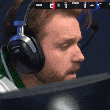 a man wearing headphones and a microphone looks at a monitor with a scoreboard that says planted