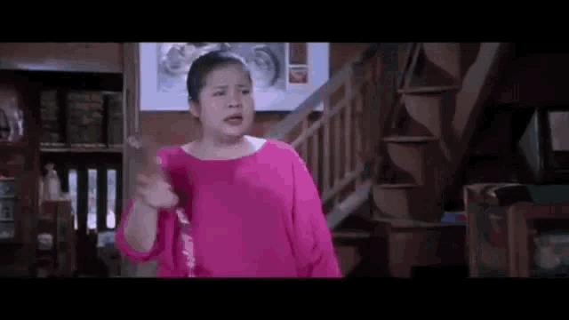 a woman in a pink shirt is standing in front of a staircase in a room .