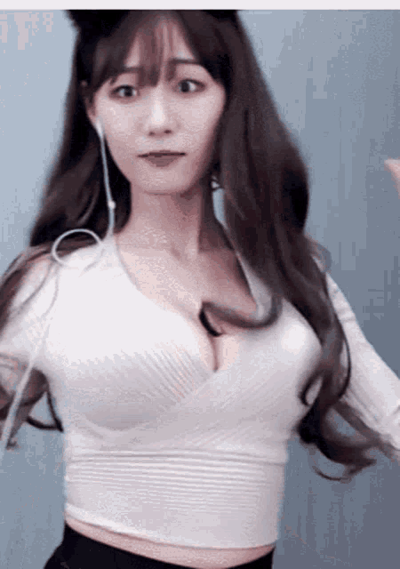 a woman wearing headphones and a white crop top is dancing on a webcam .