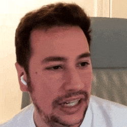a man with a beard and ear buds is sitting in a chair and making a funny face .