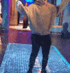a man in a sweater and black pants is standing on a tiled floor with his arms outstretched .