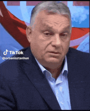 a man in a suit and white shirt is making a funny face while sitting in front of a flag .