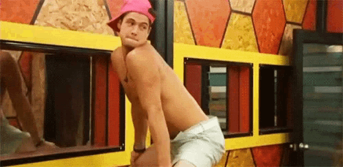 a shirtless man wearing a pink hat and shorts is standing in front of a window .