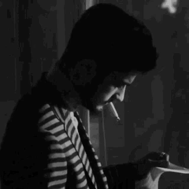 a man in a striped shirt and tie is smoking a cigarette while reading a book .