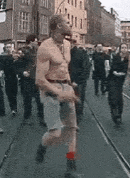 a man without a shirt is running down a street with a group of people behind him .