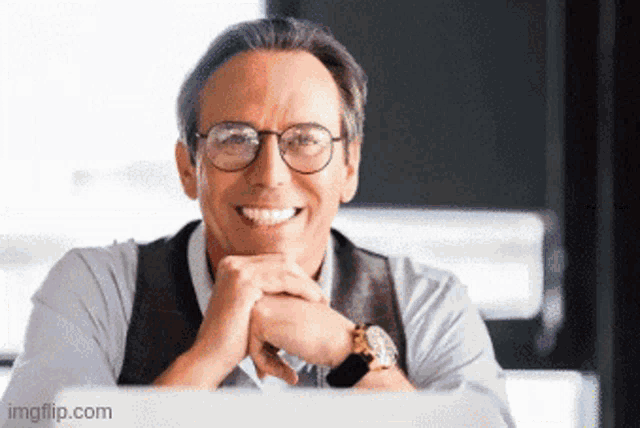 a man wearing glasses is smiling while sitting at a desk