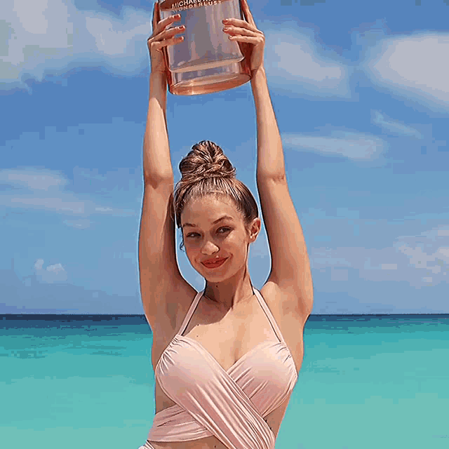 a woman in a bikini is holding a bottle of michael kors perfume over her head