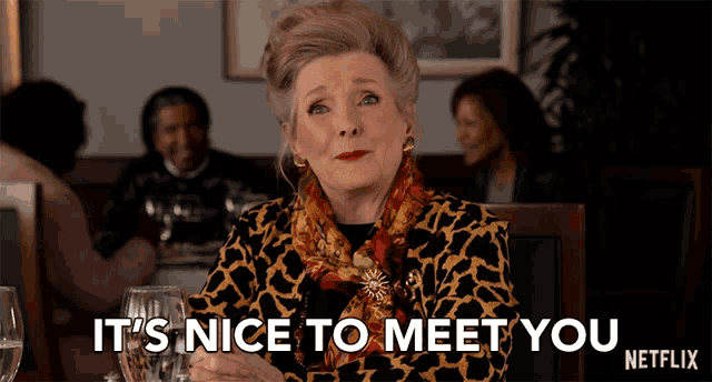 a woman is sitting at a table with a glass of wine and says it 's nice to meet you