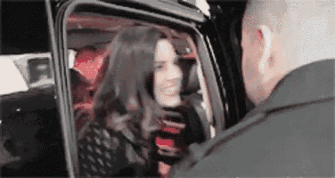 a woman is getting out of a car with a man standing behind her .