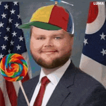 a man in a suit and tie is holding a rainbow lollipop in front of an american flag .