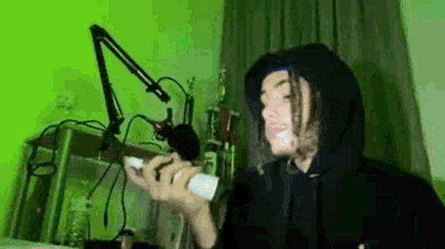 a person in a hoodie is holding a microphone in front of a microphone stand .