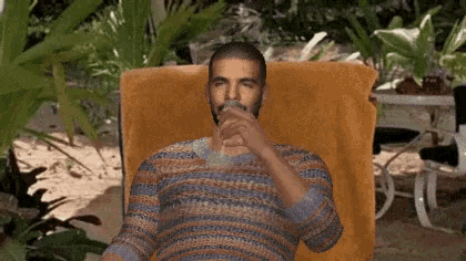 a man in a striped shirt is sitting in a chair drinking a drink