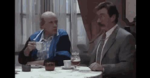 two men are sitting at a table drinking coffee .