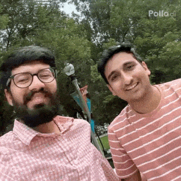 two men are posing for a picture together in a park . one of the men has a beard and glasses .