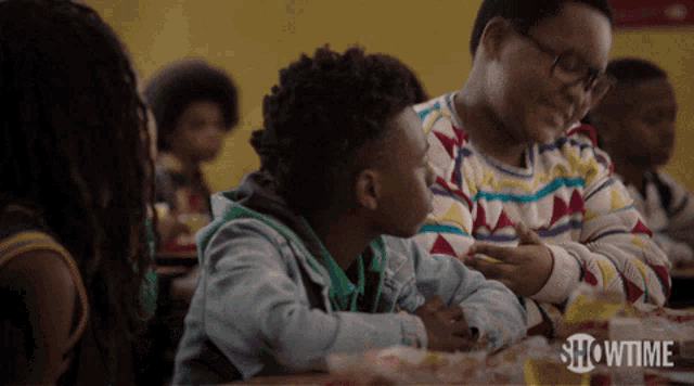 a group of children are sitting at a table with showtime written on the bottom right