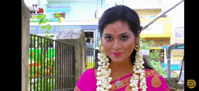 a woman in a pink saree with a garland of white flowers around her neck