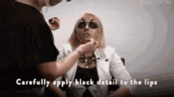 a woman is applying black makeup to her lips .