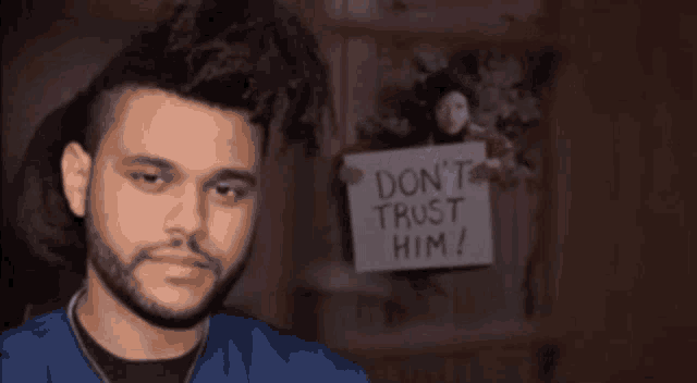 a man with a beard stands in front of a sign that says " don 't trust him "