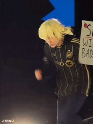 a person wearing a yellow wig and a black jacket with the letter m on it