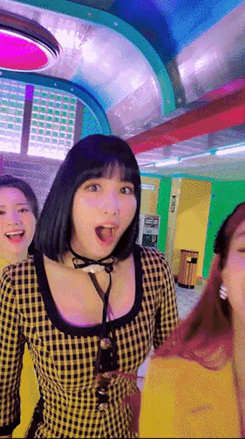 a woman wearing a plaid shirt and a bow tie is standing in a room with other women