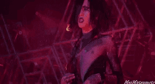a man in a fishnet top is singing into a microphone on stage .