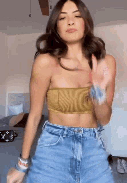 a woman wearing a crop top and jeans is dancing in a bedroom .
