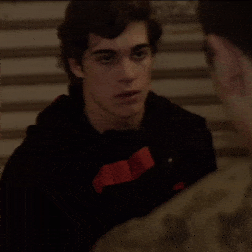 a man in a camouflage shirt is talking to another man in a dark room