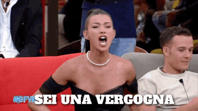 a woman with a pearl necklace is sitting on a red couch with the words sei una verogna below her