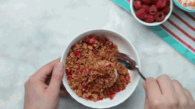 a person is scooping granola into a bowl with raspberries