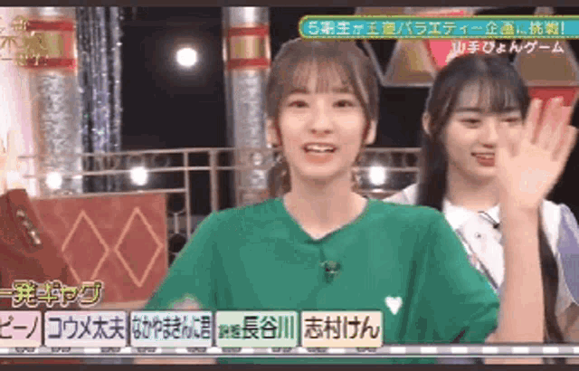 two young women are standing next to each other on a stage and one of them is waving her hand .