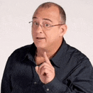 a bald man wearing glasses and a blue shirt is pointing his finger up .