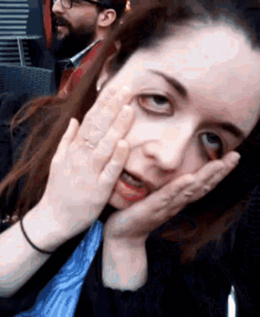 a woman is covering her face with her hands and a man is behind her