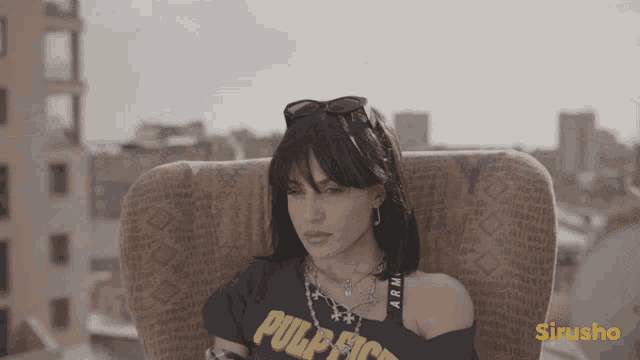 a woman wearing a pulp fiction shirt is sitting on a chair