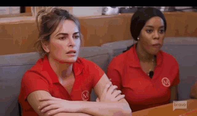two women are sitting at a table with their arms crossed and looking at something .