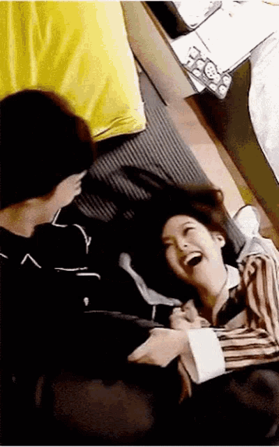 a man and a woman are laying on a bed laughing and playing with each other .