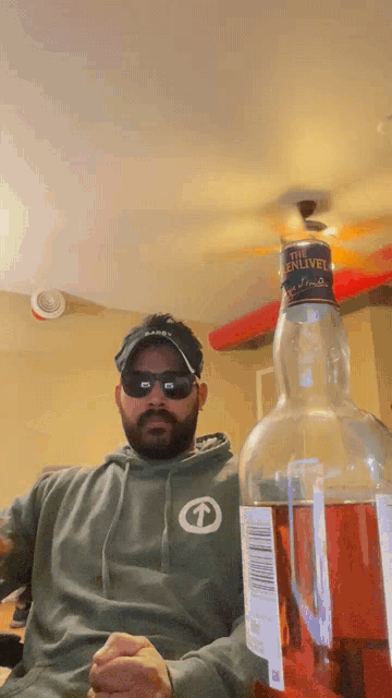 a man wearing sunglasses sits next to a bottle of the enliven
