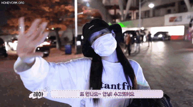 a woman wearing a mask and a hat is waving at the camera