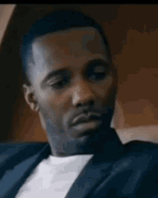 a man in a suit and white shirt is sitting on a couch looking at the camera .