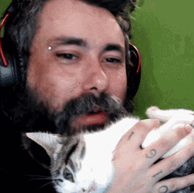 a man with a beard is holding a cat and has a tattoo on his hand that says ' t '