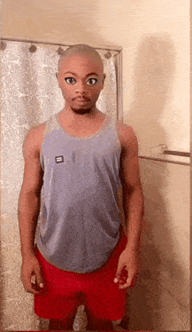 a man in a tank top and red shorts is standing in front of a shower curtain .