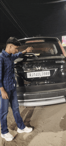 a man standing in front of a black car with a license plate that says rj14ul3988