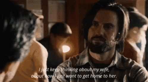 a man with a beard is talking to a woman while sitting at a table in a room .