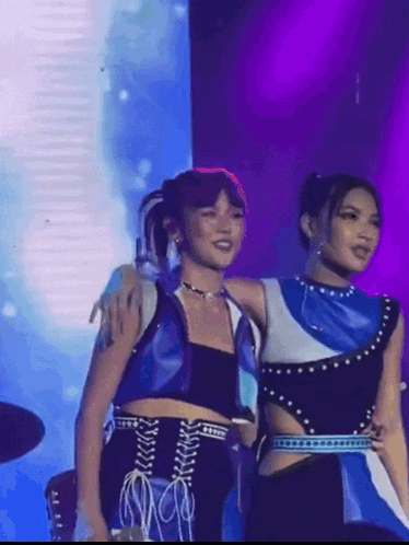 two women are standing next to each other on a stage with purple lights behind them .
